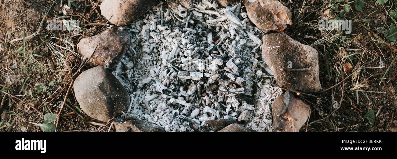 spoliatura e carboni grigi e ceneri da un fuoco estinto in falò per bambini di piccole dimensioni fatto di pietre sul terreno in estate o autunno evenin Foto Stock