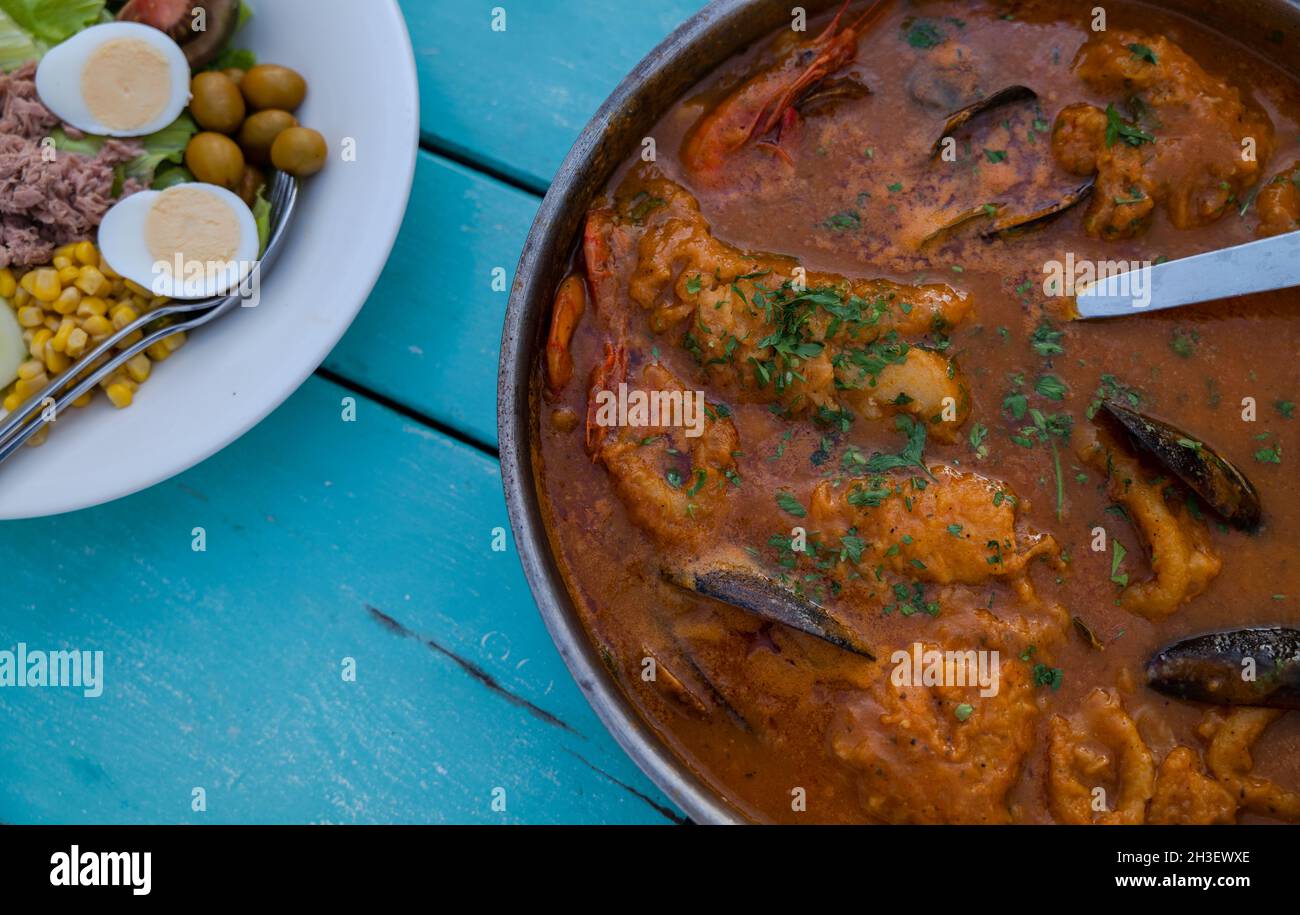 Tradizionale cucina spagnola di pesce con zuppa e insalata di verdure su tavolo di legno blu Foto Stock