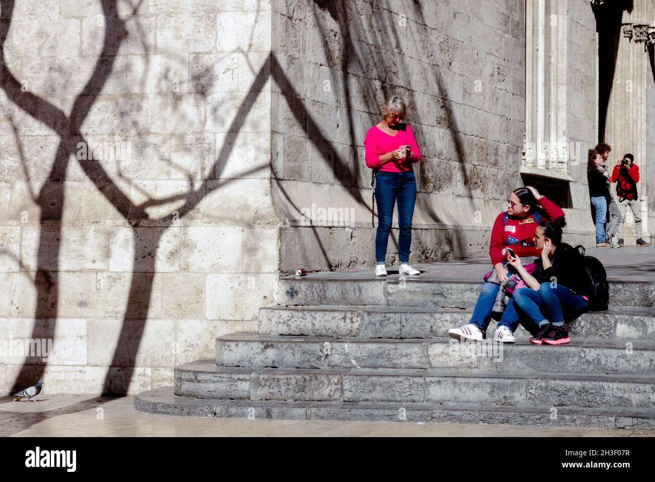 I turisti si siedono sui gradini di Calle de la Lonja Valencia Città Vecchia Spagna alberi ombre sul muro Foto Stock