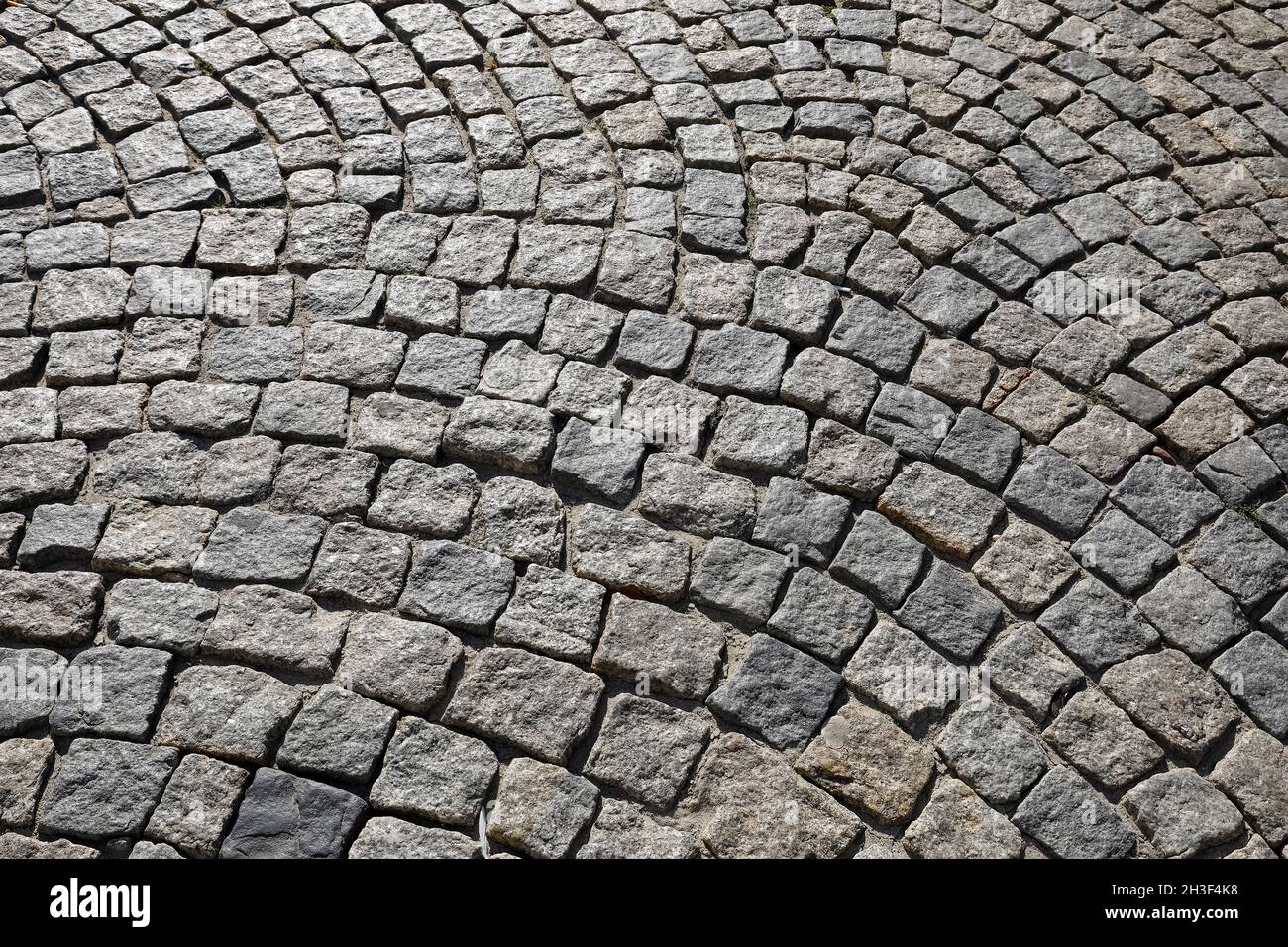 Molti piccoli blocchi di pietra impilati fianco a fianco compongono la superficie di una strada asfaltata o marciapiede. Foto Stock
