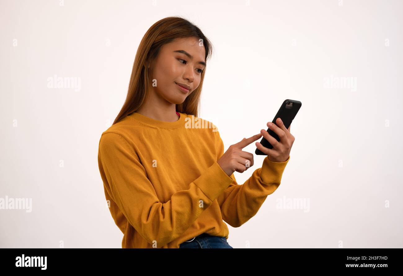 Giovane ragazza asiatica attraente sorridendo mentre usando lo smartphone in studio Foto Stock