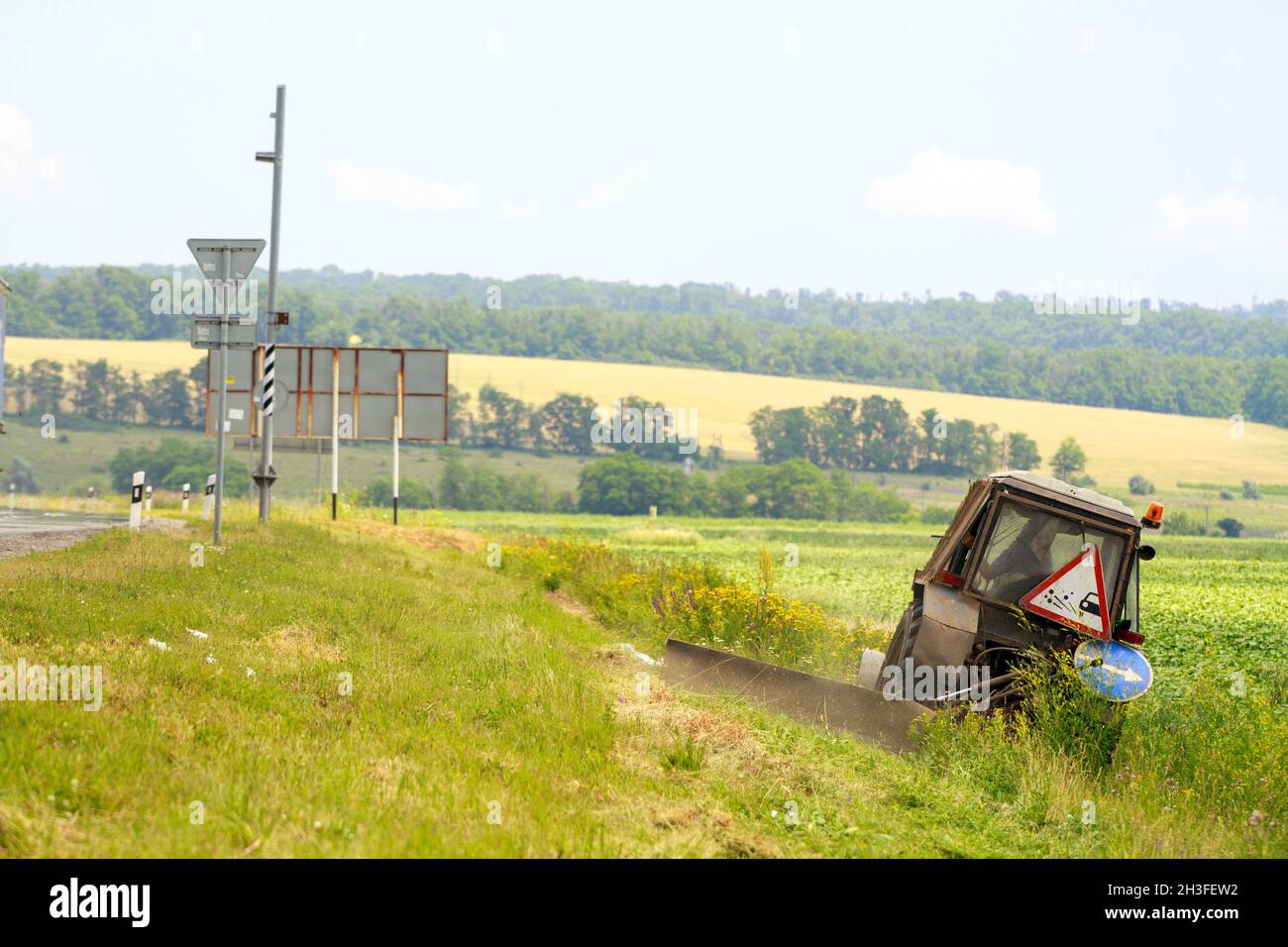 Trattore con una falciatrice meccanica la falciatura di erba sul lato della strada asfaltata Foto Stock