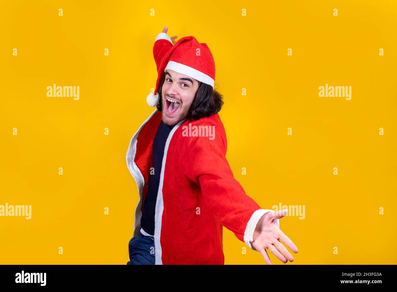 Il giovane vestito come Babbo Natale ama cantare. L'uomo sorride e a braccia aperte presenta il tuo messaggio di Natale. Foto Stock