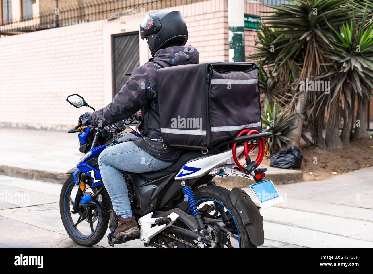 Autista di consegna del cibo con zaino su una moto che corre lungo una strada Foto Stock