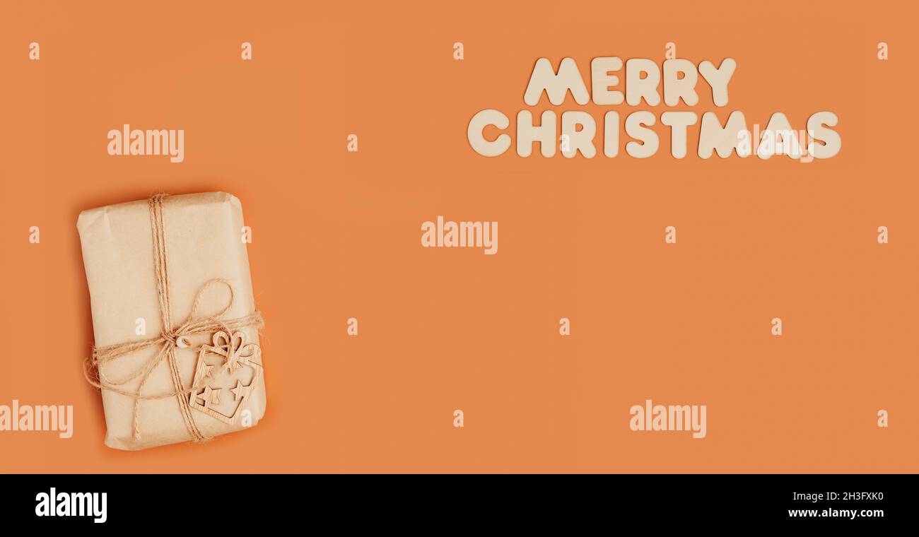 Confezione regalo confezionata in carta artigianale su sfondo arancione, banner lungo, spazio copia con testo buon Natale, vista dall'alto Foto Stock