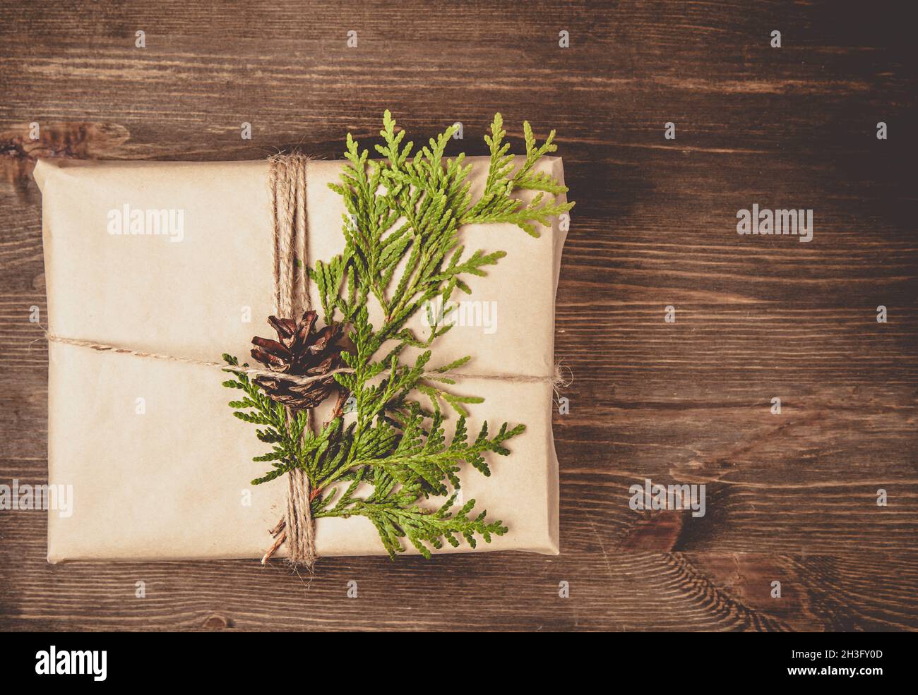 Natale zero rifiuti concetto. Accogliente confezione regalo avvolta in carta artigianale e decorata con ramificazione di cipresso verde. Sfondo di legno scuro con spazio per la copia Foto Stock