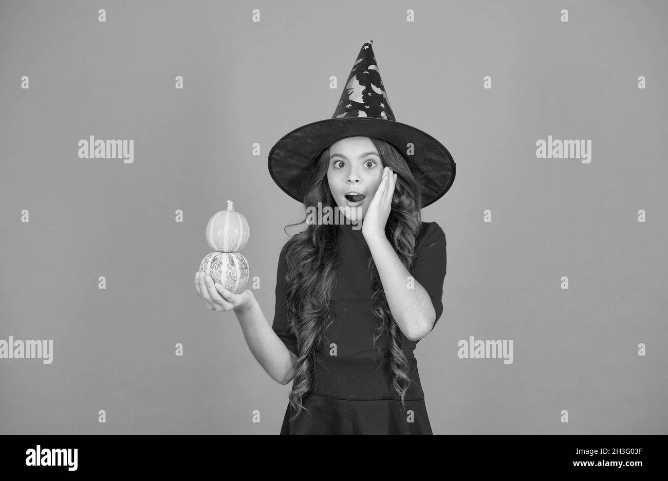 sorpresa bambino portare cappello strega. bambino con piccola zucca. teen ragazza ha lunghi capelli ricci e indossare abiti per festa celebrazione. autunno stagione vacanza Foto Stock