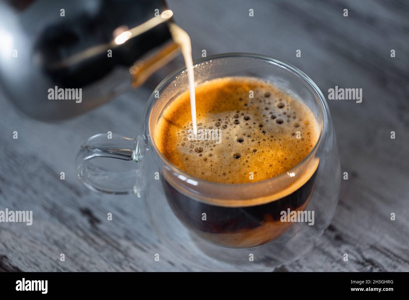 Una tazza di caffè piena di latte. Il latte caldo viene versato nel caffè del mattino Foto Stock