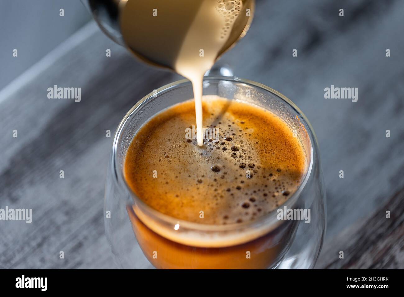 Il latte viene versato in una tazza di caffè. Caffè rinvigorente al mattino Foto Stock