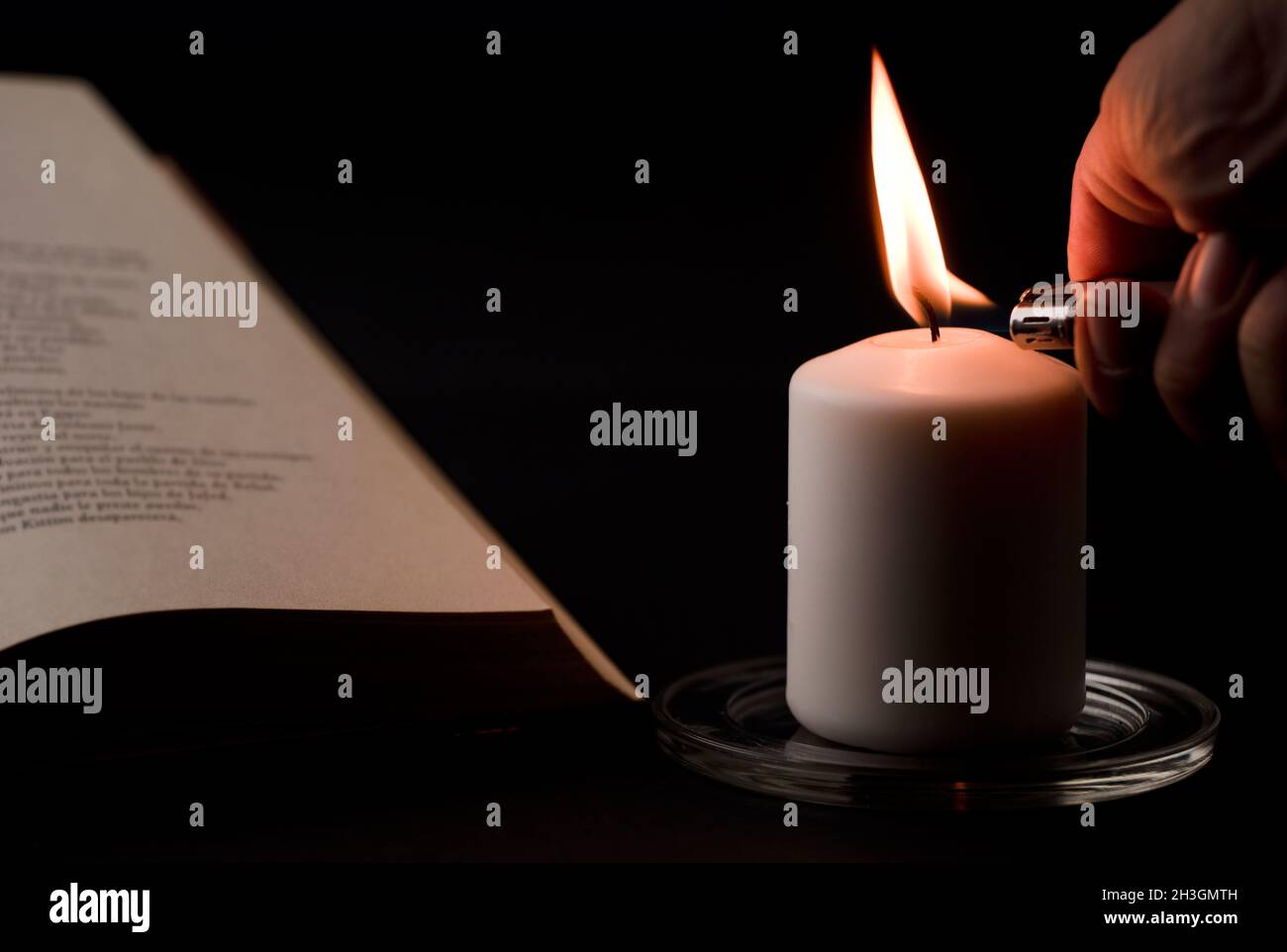 candele con fiamma, mano dell'uomo con accendino e libro da lettura sulla  scrivania, sfondo nero. (fuoco sulla candela Foto stock - Alamy