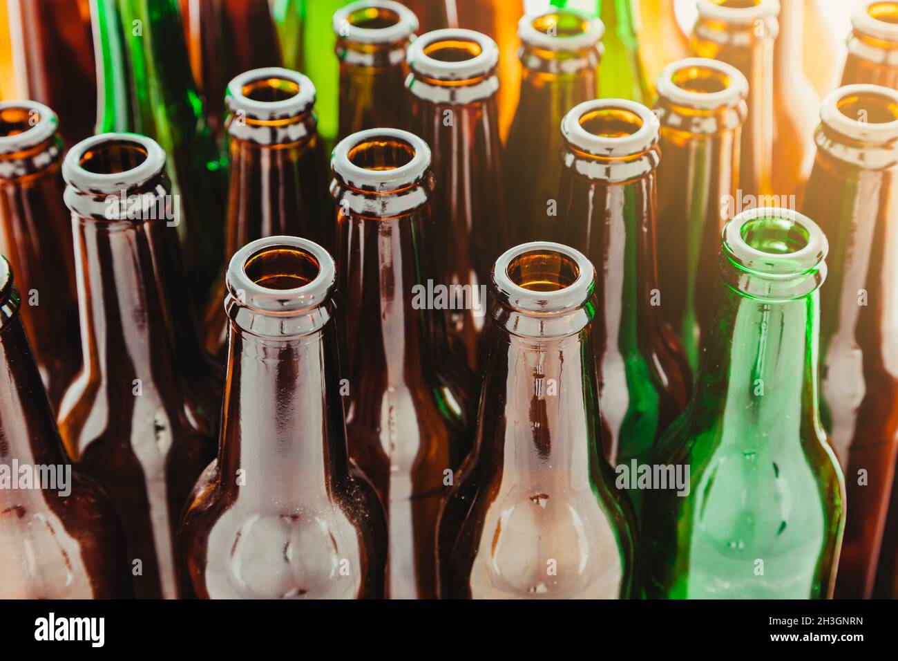 I colli di molte bottiglie di vetro verde e marrone vuote poste in posizione verticale. In un angolo dello sfondo entra un bagliore di luce. Foto Stock