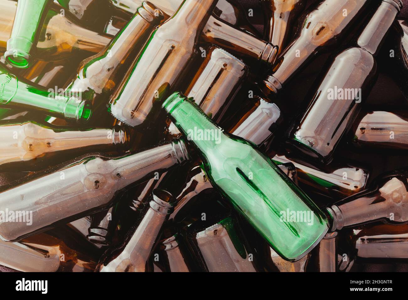 Un mucchio di bottiglie di vetro verde e marrone vuote. Da un angolo entra un bagliore di luce. Foto Stock