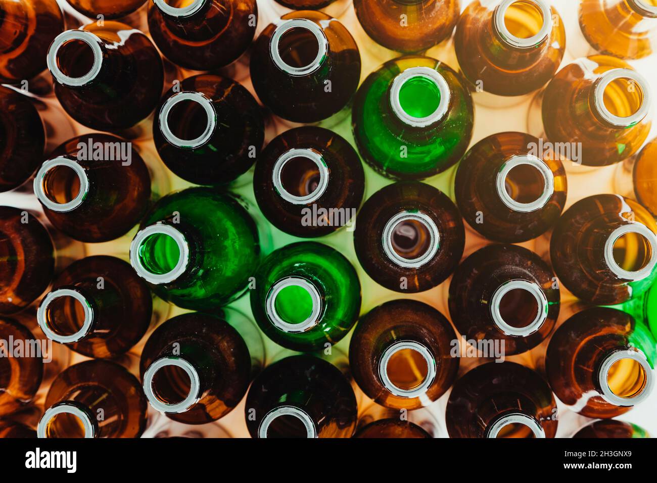 Visto dall'alto, molte bottiglie di vetro verde e marrone vuote sono in posizione verticale. In un angolo entra un bagliore di luce. Foto Stock