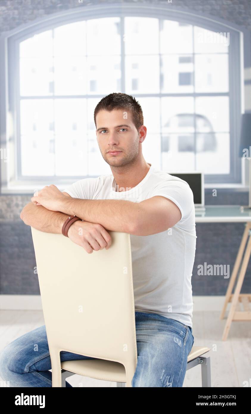 Giovane uomo in jeans seduto al contrario sulla sedia Foto stock - Alamy