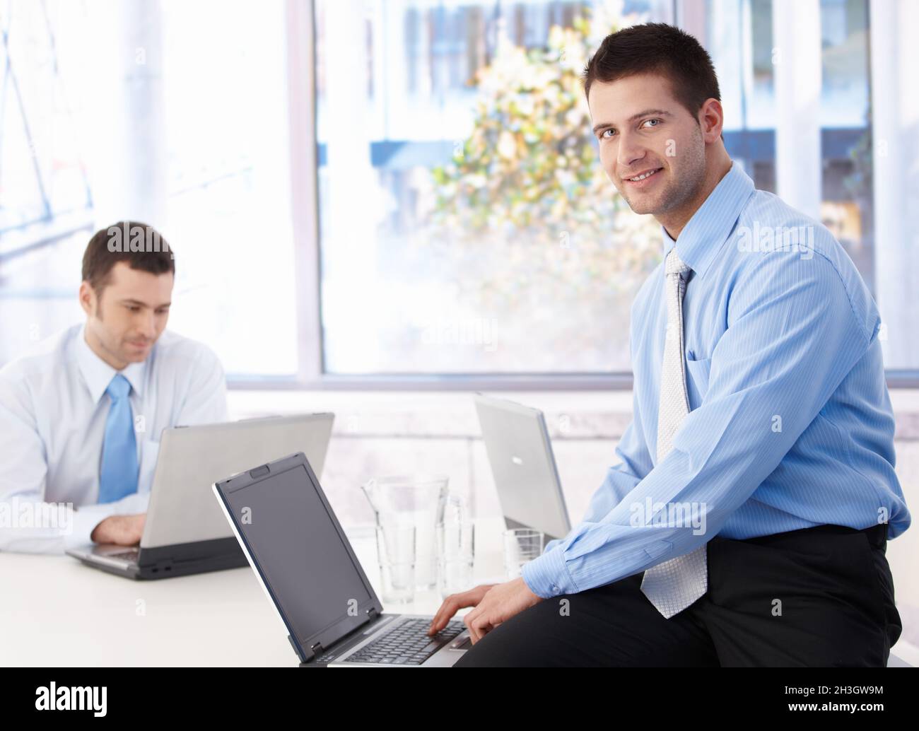 Giovane uomo d'affari che usa un notebook sorridendo in ufficio Foto Stock