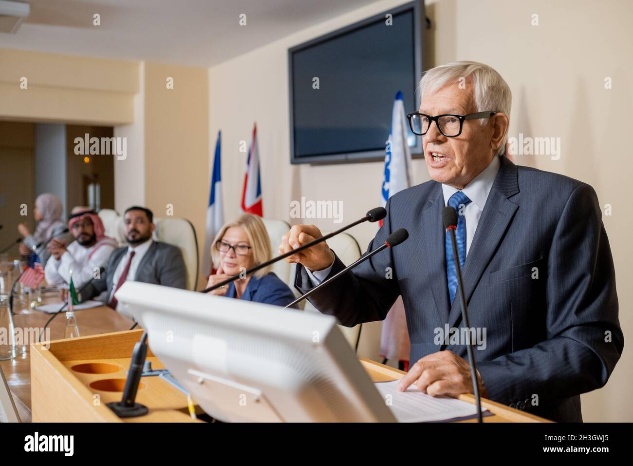 Uomo politico emozionale anziano dai capelli bianchi in occhiali e vestire la mano gesturante, dando un discorso ispiratore alla conferenza stampa Foto Stock