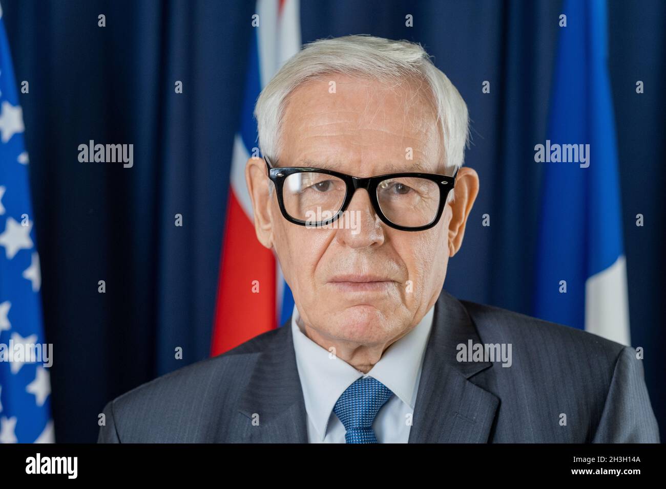 Ritratto di uomo politico serio e fiducioso in occhiali in piedi contro bandiere e tende blu scuro Foto Stock
