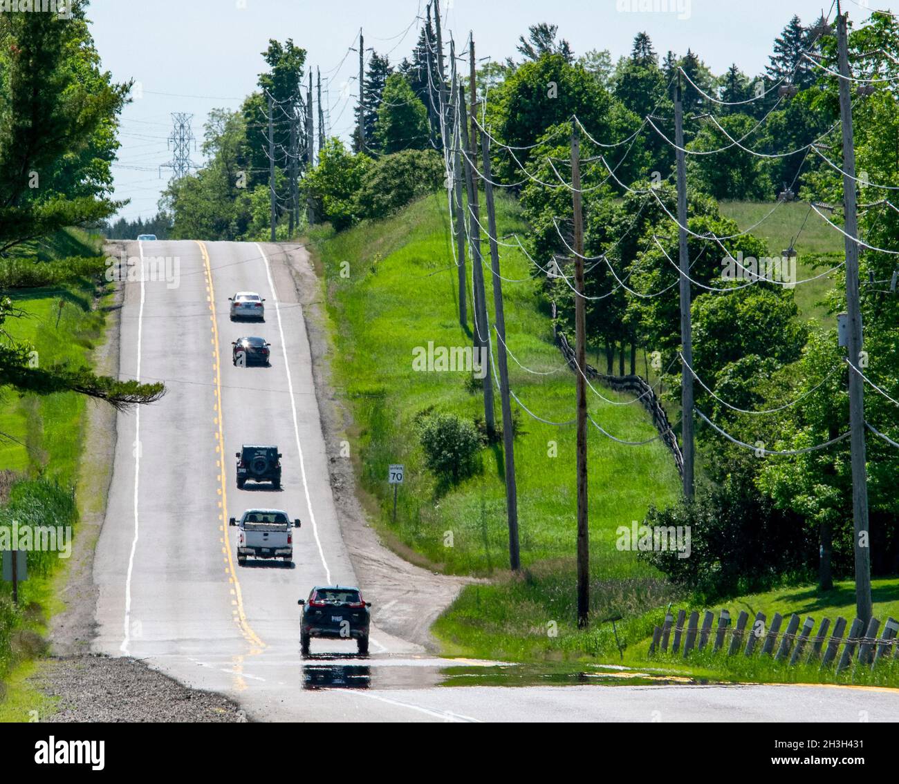 Una strada di campagna con veicoli a distanza e un miraggio all'orizzonte, in una calda giornata estiva in Ontario, Canada - stock Photography Foto Stock