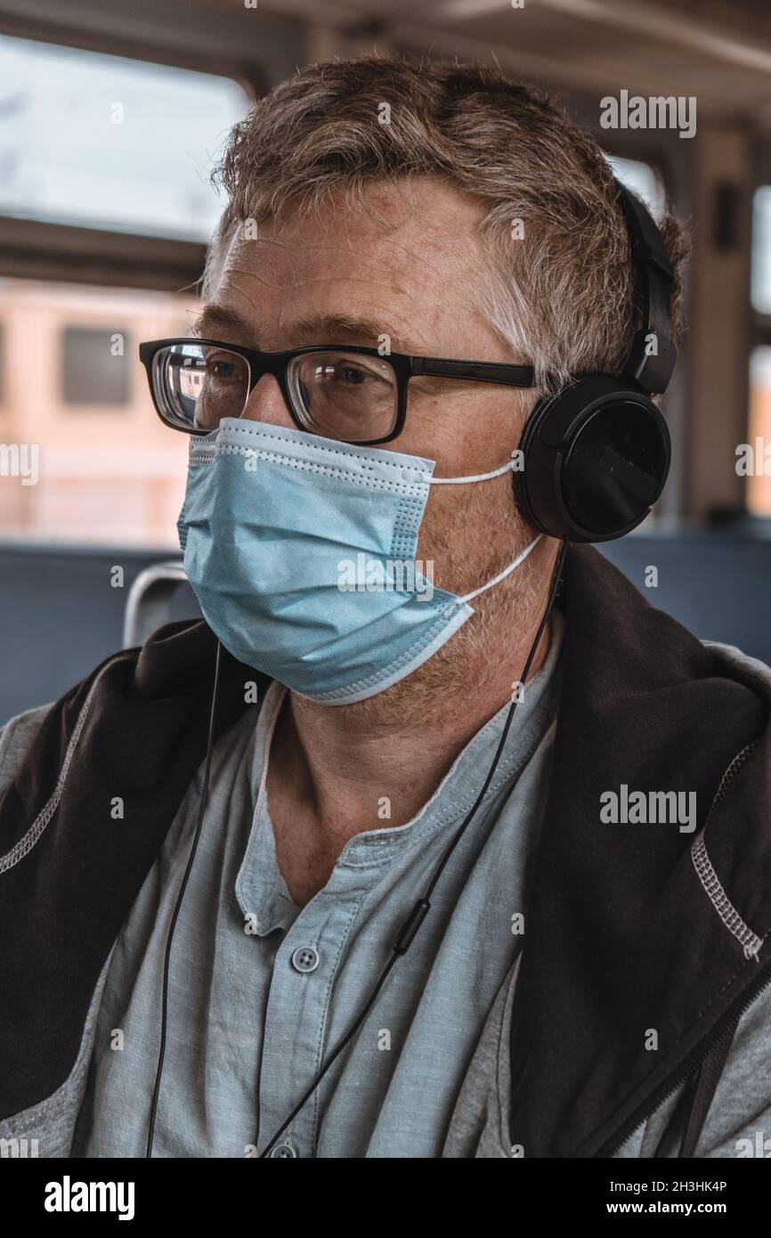 Primo piano ritratto di un uomo adulto che indossa cuffie e occhiali con una maschera medica protettiva sul suo volto nei trasporti pubblici. Distanza sociale. Foto Stock