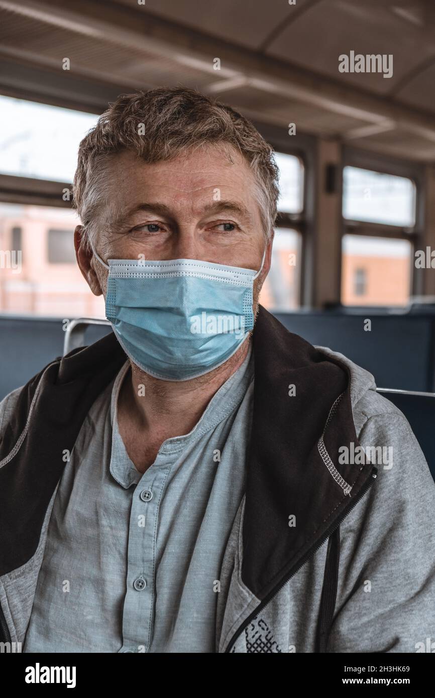 Ritratto di un uomo adulto serio con una maschera medica protettiva sul suo volto all'interno di un trasporto pubblico. Distanza sociale durante la pandemia del coronavirus. Foto Stock