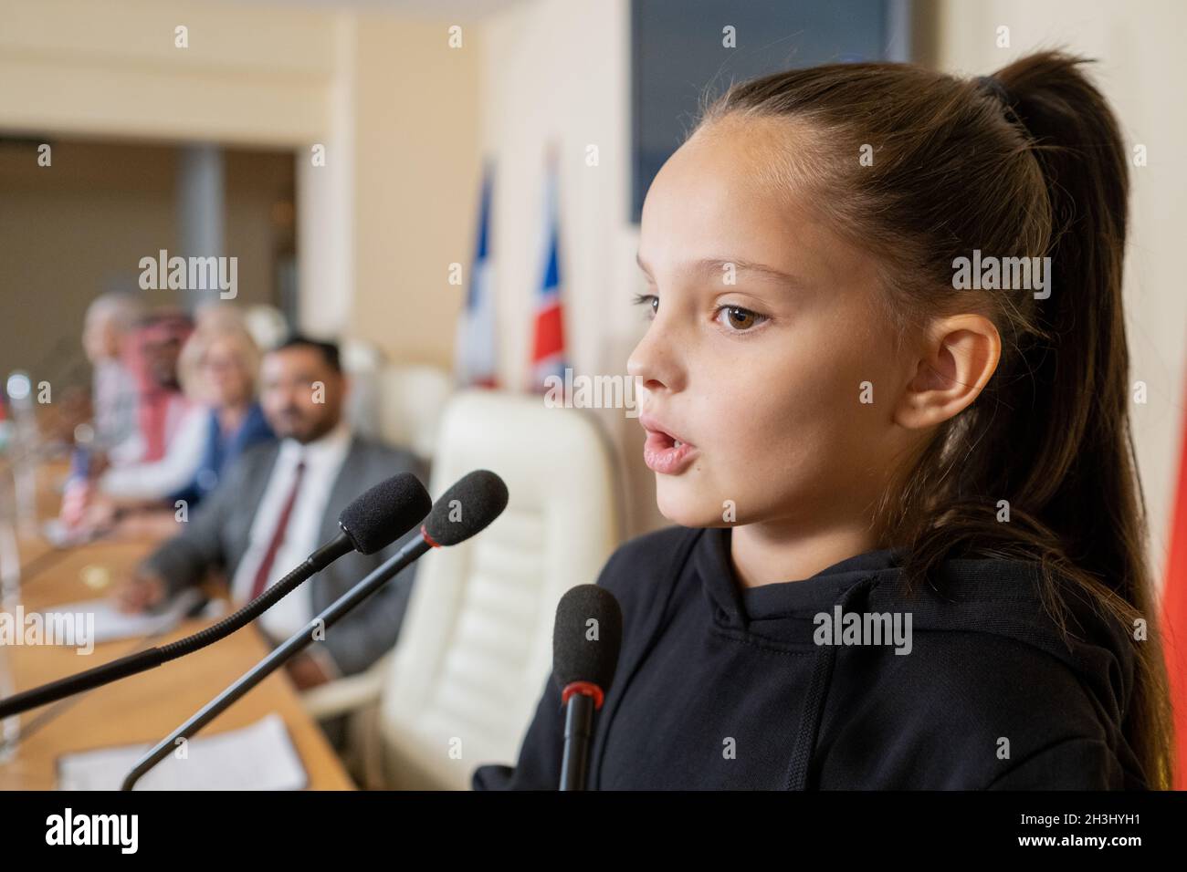 Piccolo attivista con ponytail che parla nel microfono mentre si rivolge alla conferenza di fronte al pubblico congressuale Foto Stock