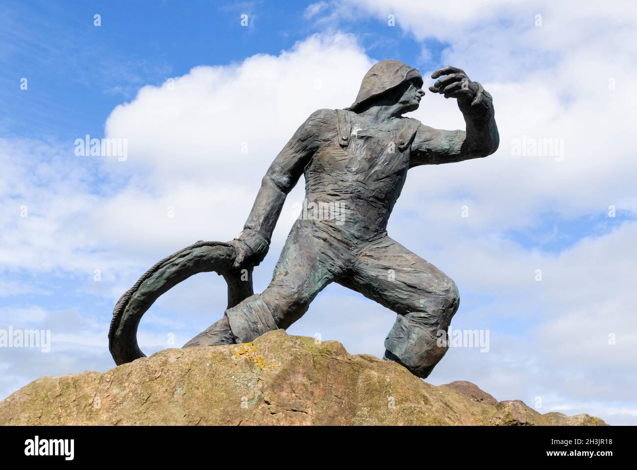 Il salvataggio una statua di bronzo di un uomo che getta una cintura di salvataggio su una base di pietra grezza vicino alla stazione di salvagente in Seahouses Northumberland Inghilterra UK Foto Stock