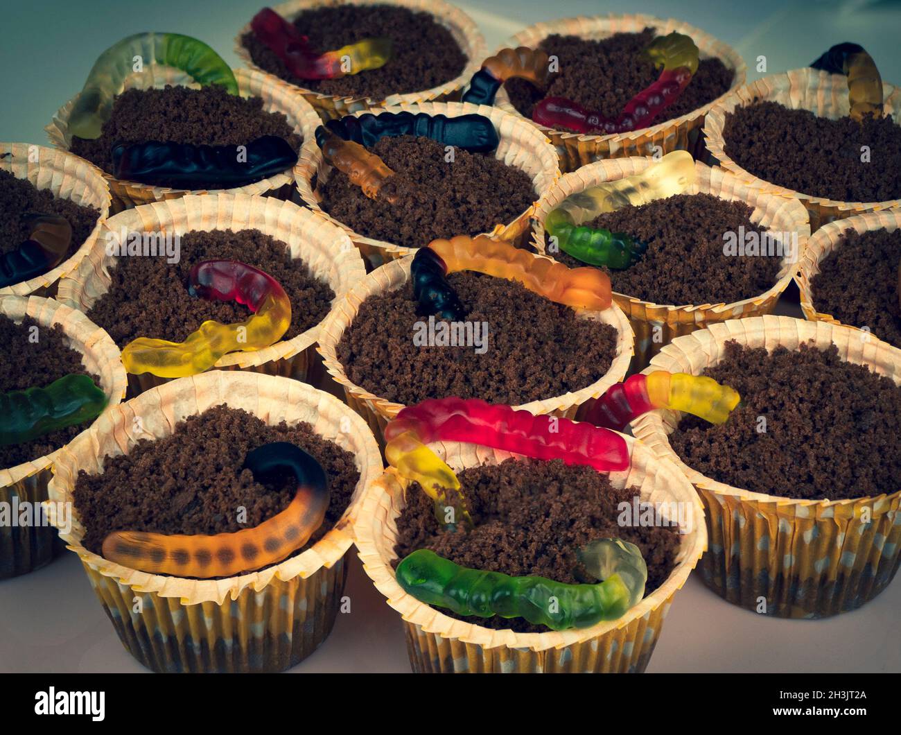 Tortini di Halloween con vermi colorati di gelatina che escono da briciole come se fosse terreno. Cibo creativo per le vacanze. Disgustoso, spooky, dessert Foto Stock