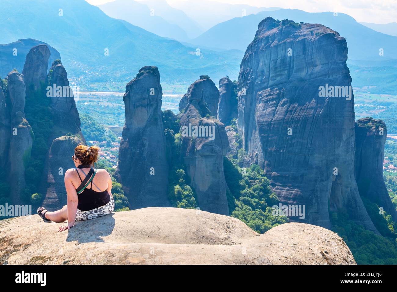 Donna turistica seduta sulla cima della scogliera e guardando la valle. Meteora, Grecia Foto Stock