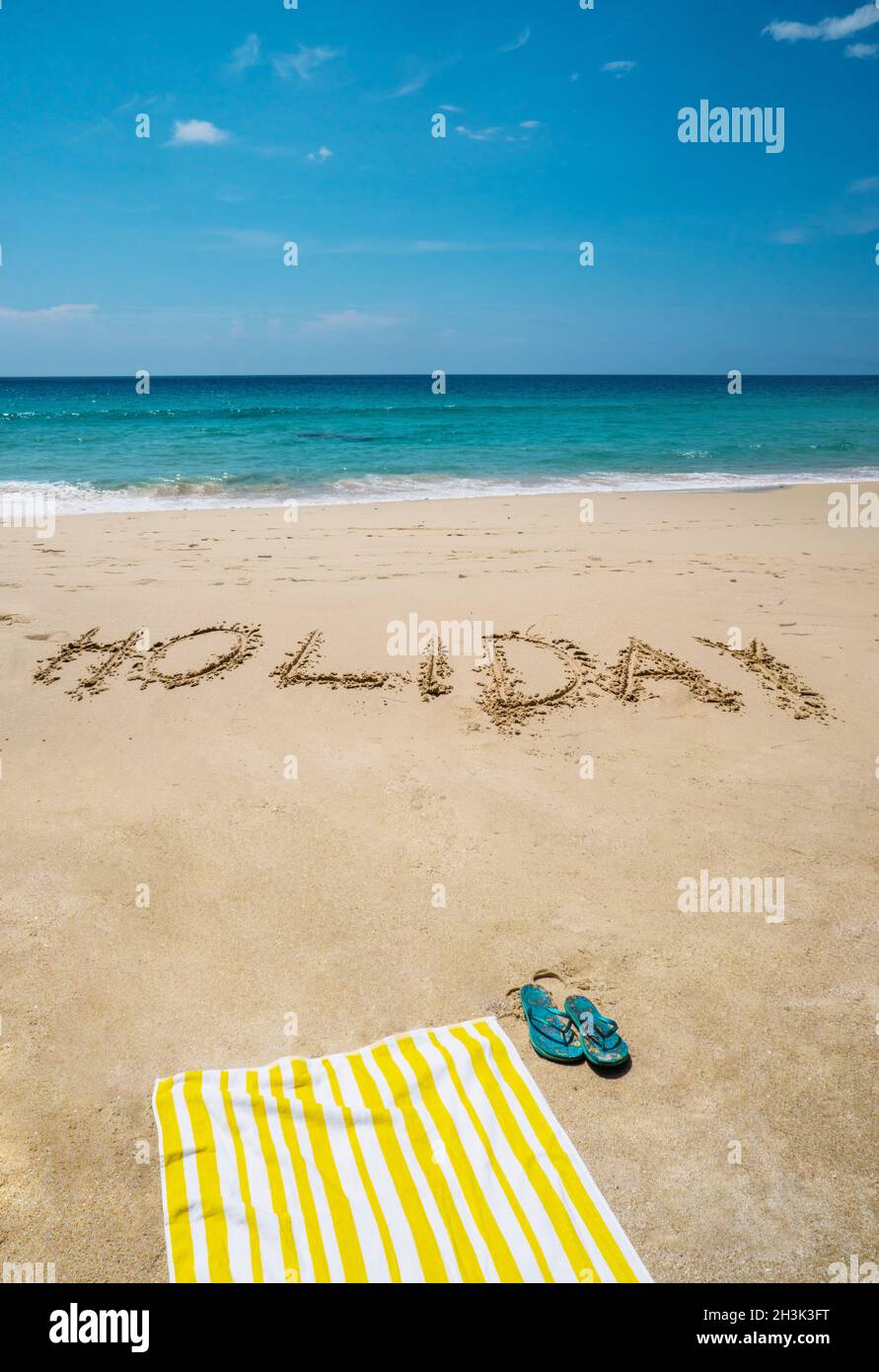 Vacanza scritta sulla spiaggia con asciugamano e infradito sul mare Foto Stock