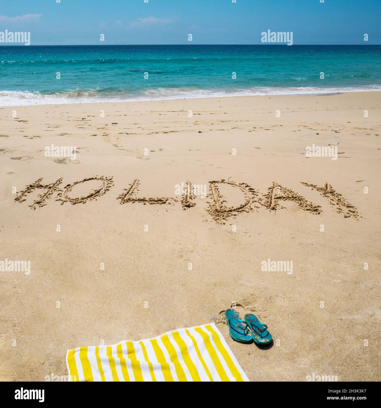 Vacanza scritta sulla spiaggia con asciugamano e infradito sul mare Foto Stock