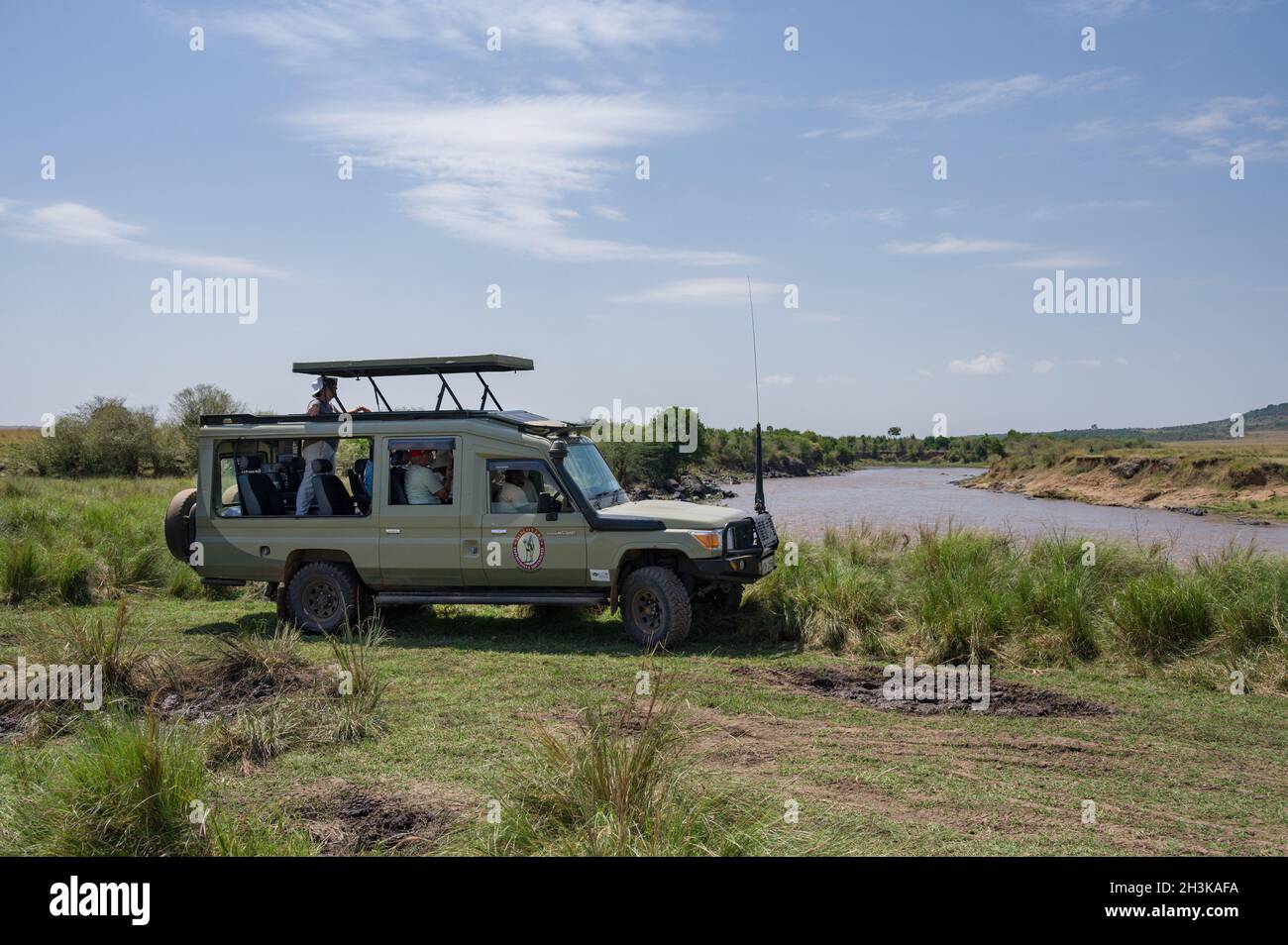 Un 4x4 Toyota Landcruiser safari veicolo con i turisti parcheggiati dal fiume Mara in attesa di animali per attraversare, Masai Mara, Kenya Foto Stock