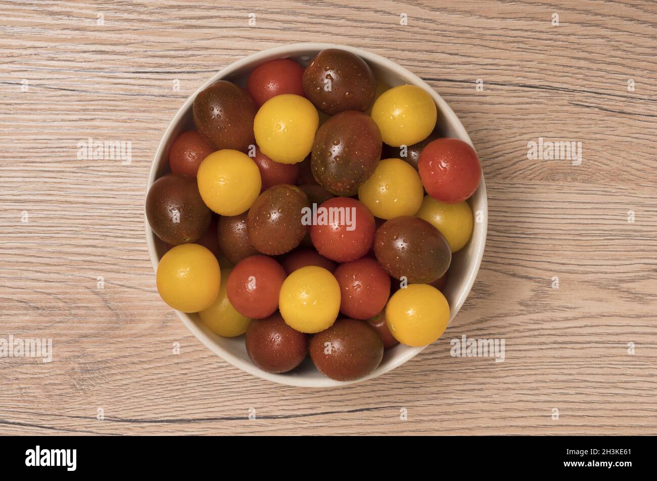 Pomodori ciliegini, rosso, giallo e kamato nel recipiente di ceramica su sfondo di legno. Vista dall'alto. Foto Stock