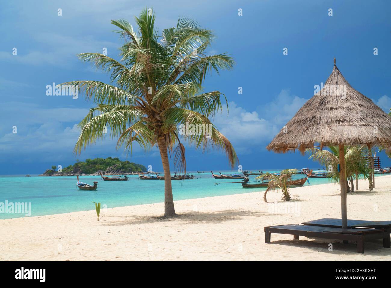 Spiaggia tropicale con sdraio, ombrelloni, barche e palme Foto Stock