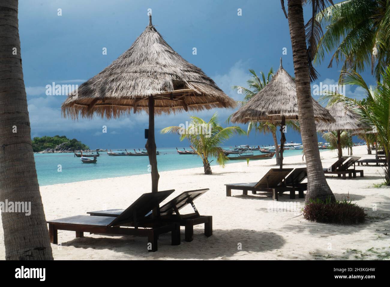 Spiaggia tropicale con sdraio, ombrelloni, barche e palme Foto Stock