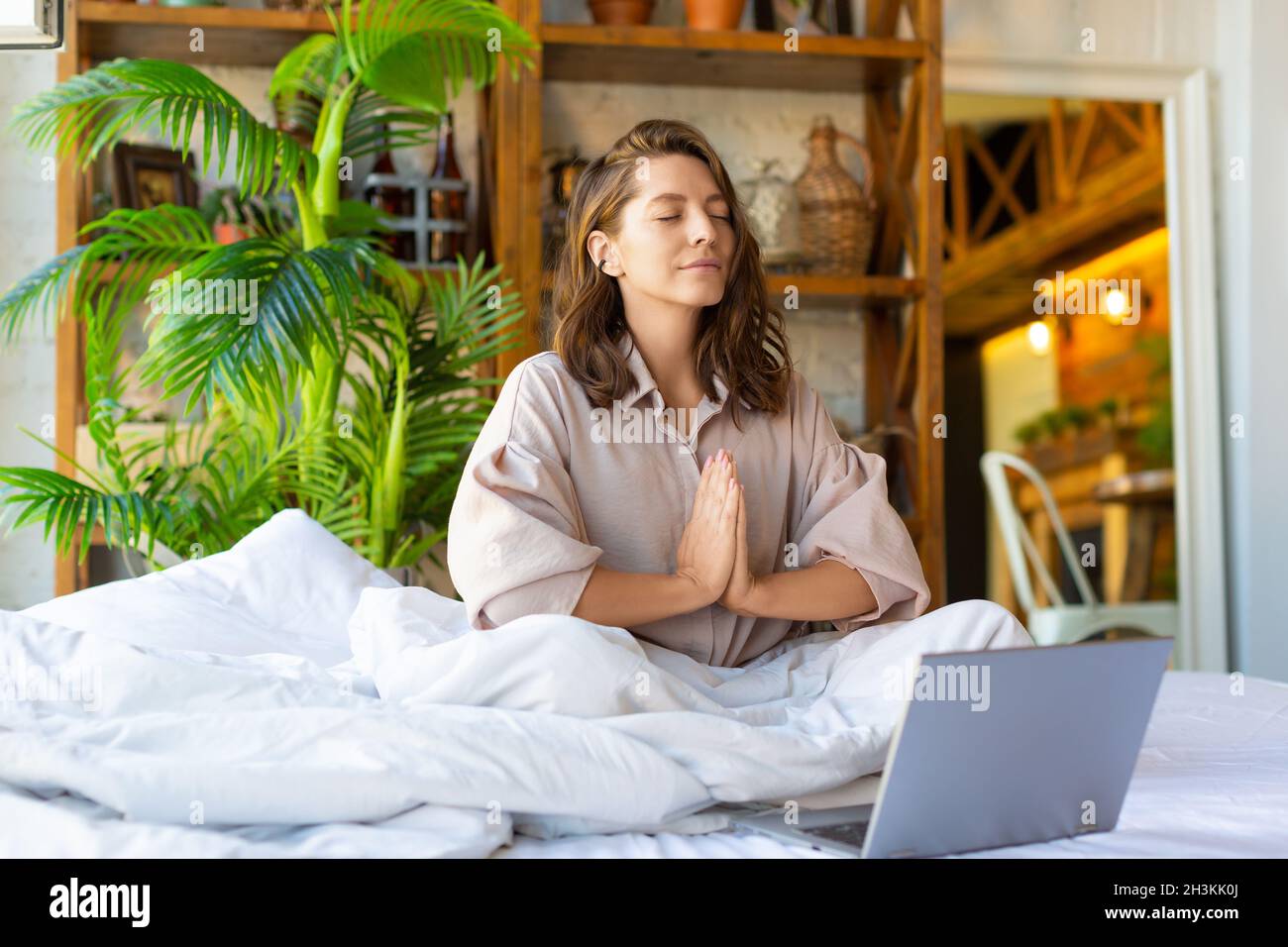 Giovane donna adulta meditating a letto davanti al monitor del portatile - concetto di ripristinare la forza e l'energia mentale attraverso la pratica di yoga. Foto Stock