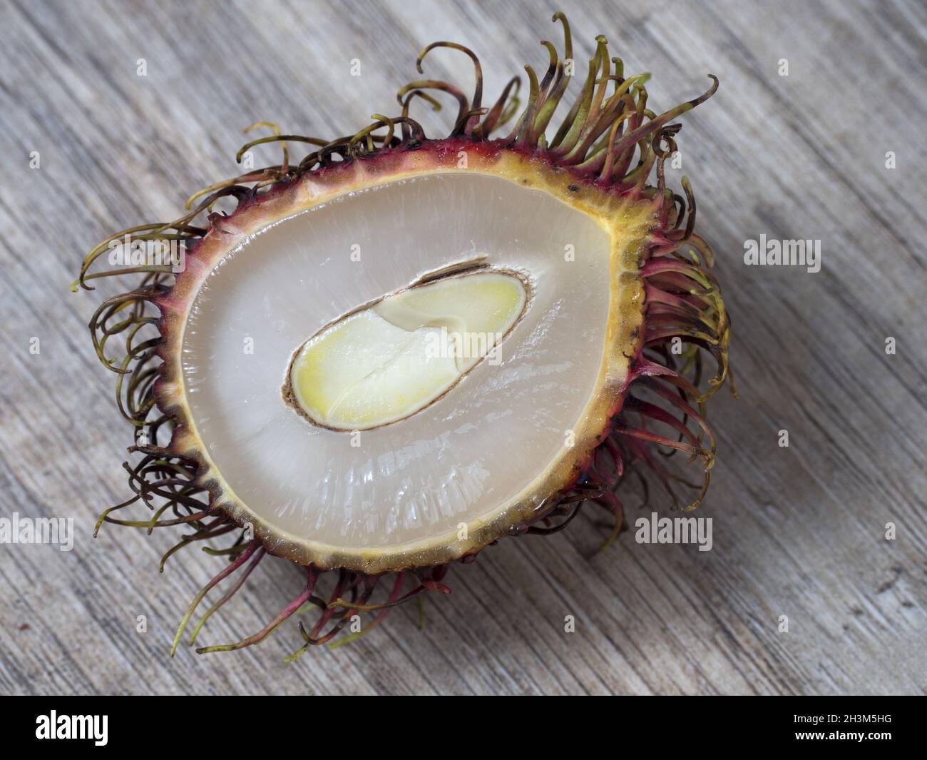 Metà di un rambutano su sfondo di legno. Foto Stock