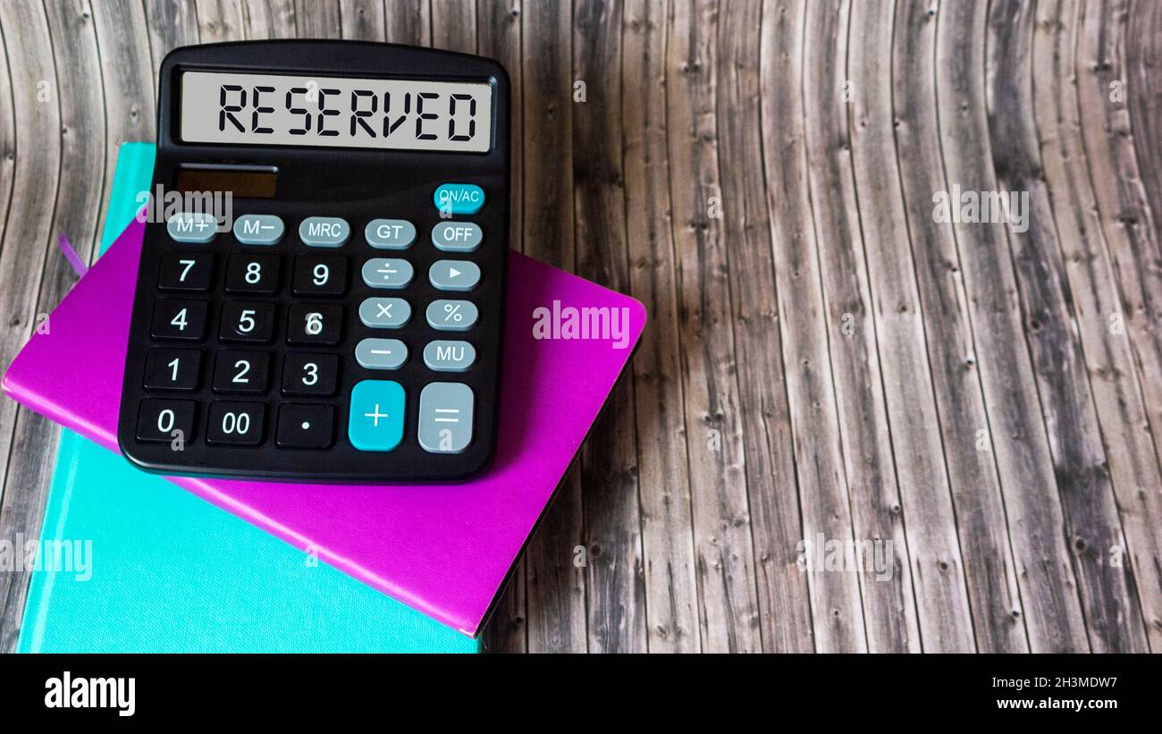 Sul display della calcolatrice viene visualizzato riservato per. I notepad colorati giacciono su un tavolo di legno Foto Stock