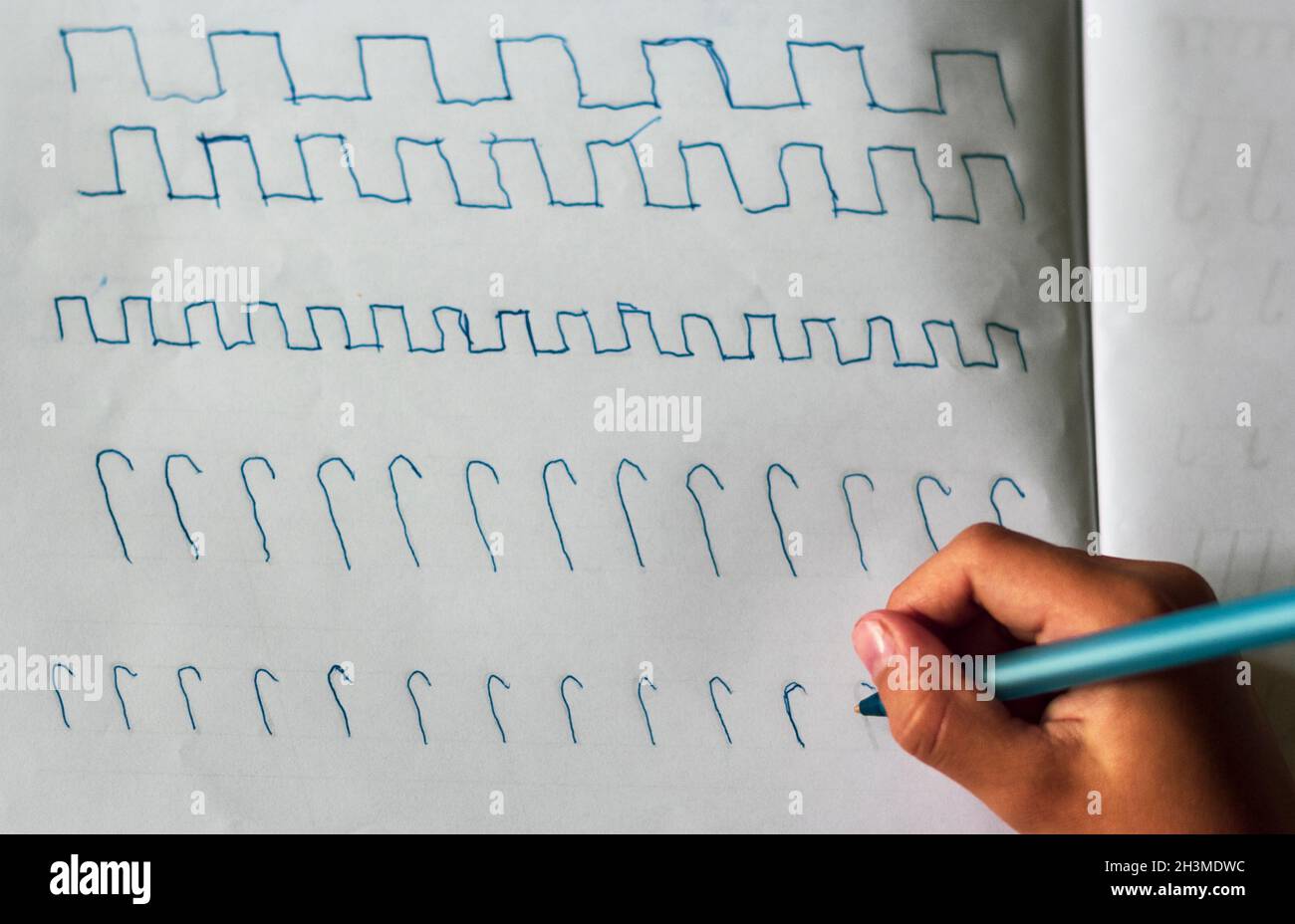 Le mani dei bambini con una penna blu sul tavolo con un foglio di carta scrive squiggles. Vista dall'alto. Foto Stock