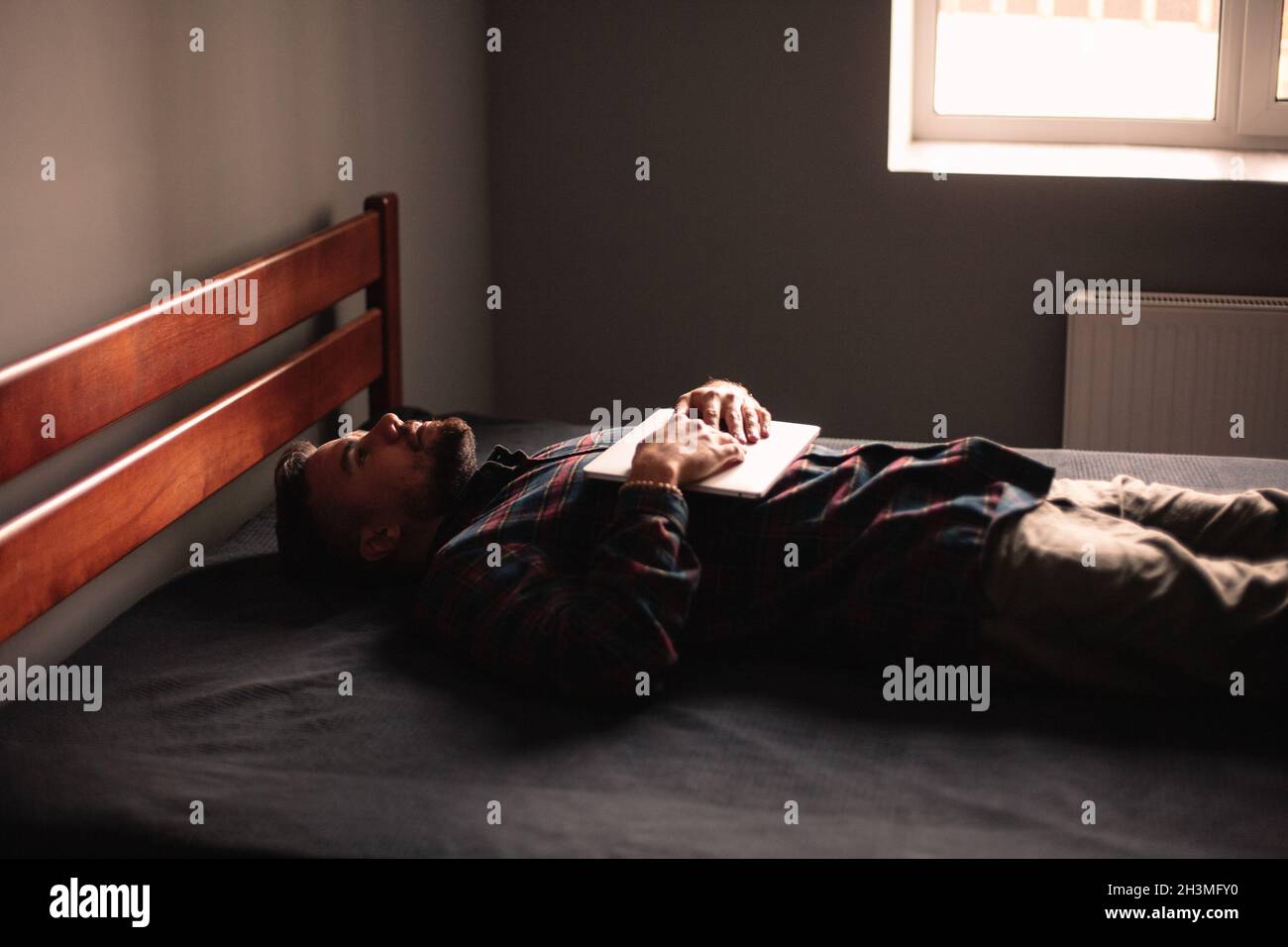 Uomo esausto con computer portatile sdraiato a casa Foto Stock