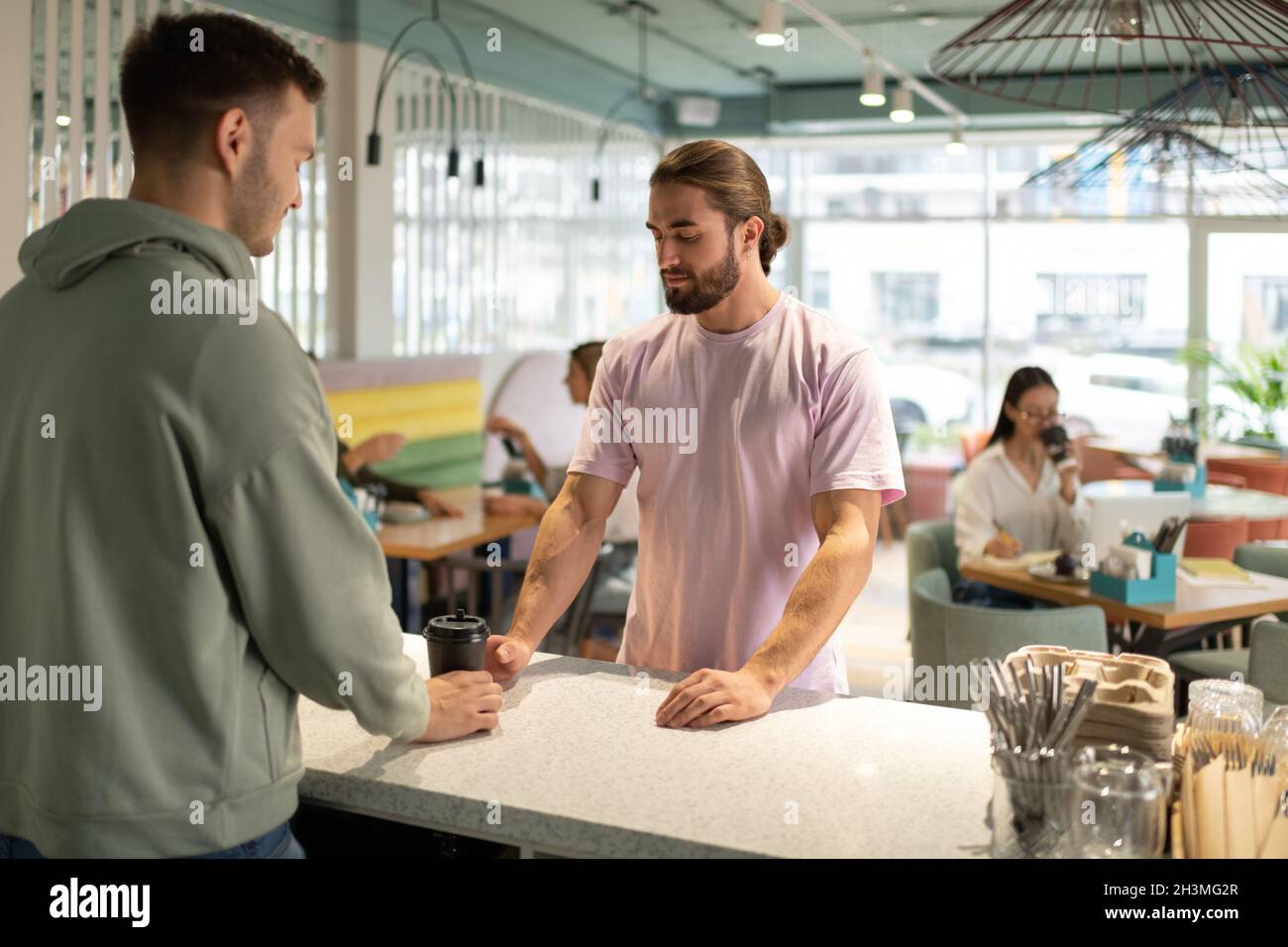Cliente maschio bearded che prende il caffè per andare dal barista durante la visita nel caffè moderno Foto Stock