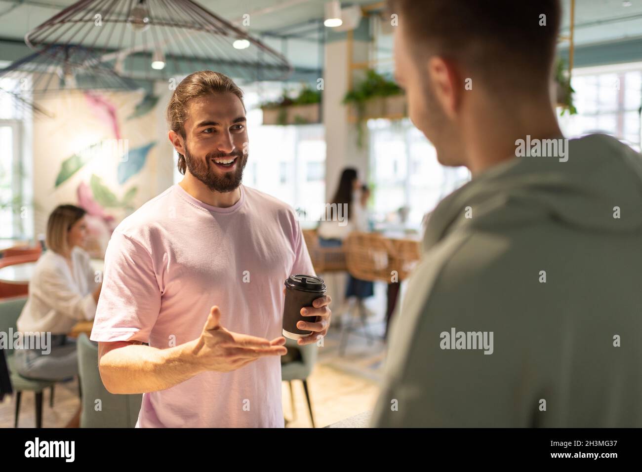 Uomo felice con il caffè per andare sorridente e parlare con il barista maschile in caffetteria Foto Stock