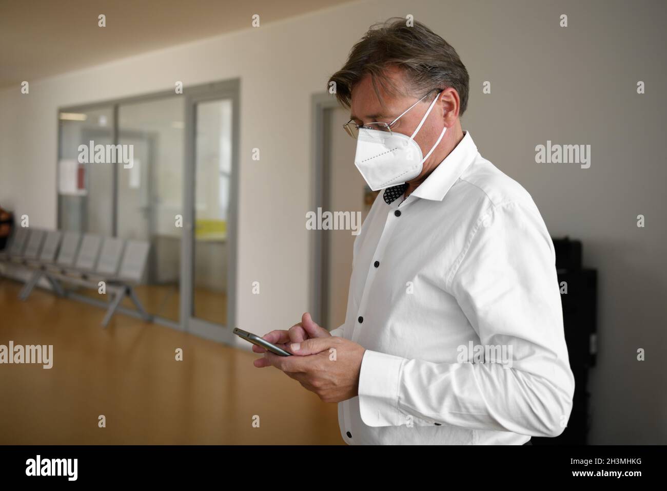 Uomo adulto in occhiali, indossare maschera protettiva contro le malattie infettive trasmissibili e come protezione contro l'influenza in ufficio pubblico, utilizzando e. Foto Stock