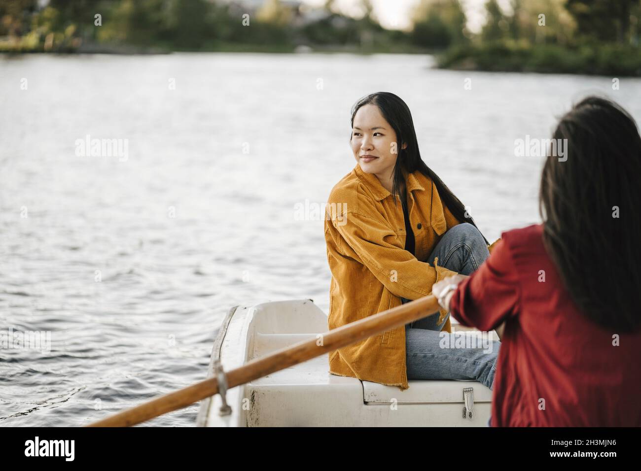 Donna che guarda via mentre femmina amico barca a remi sul lago Foto Stock