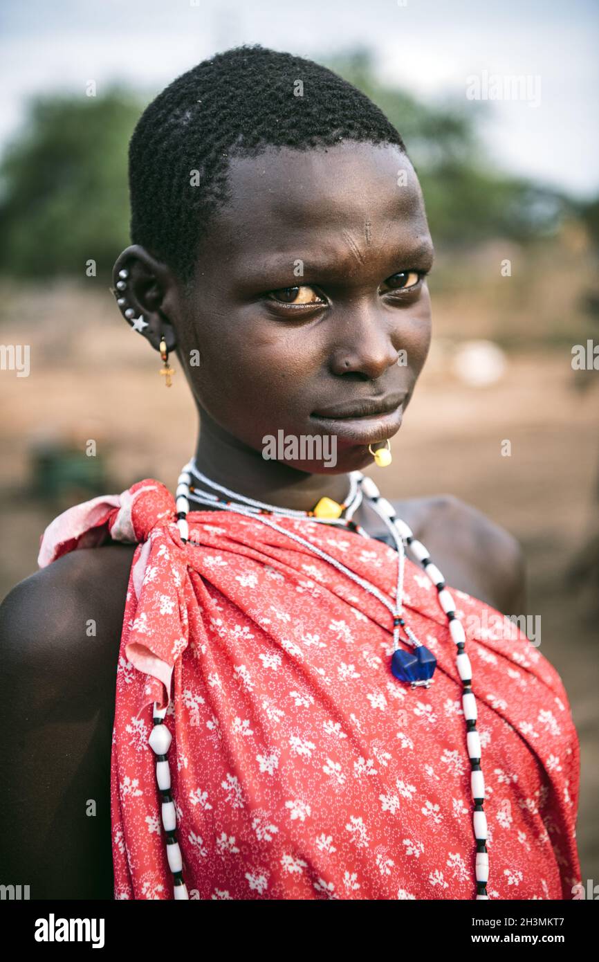 Tribù TOPOSA, SUDAN DEL SUD - 12 MARZO 2020: Adolescente con capelli corti indossando abiti e accessori luminosi e guardando camer Foto Stock