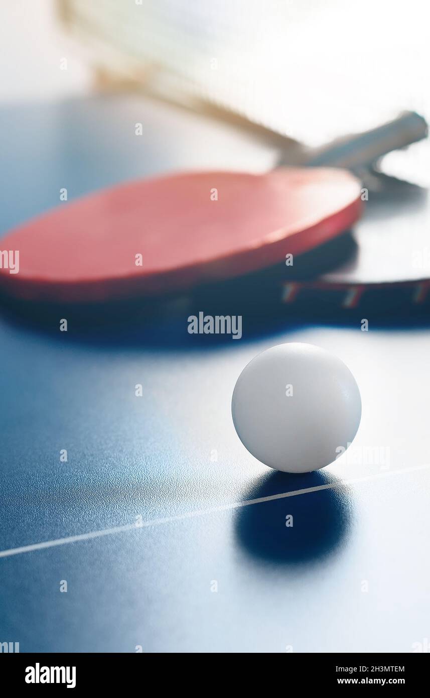 Due racchette da tennis e una palla bianca si trovano su un tavolo da tennis vicino alla rete. Attività ricreative attive e giocare a ping pong. Background sportivo. Foto Stock
