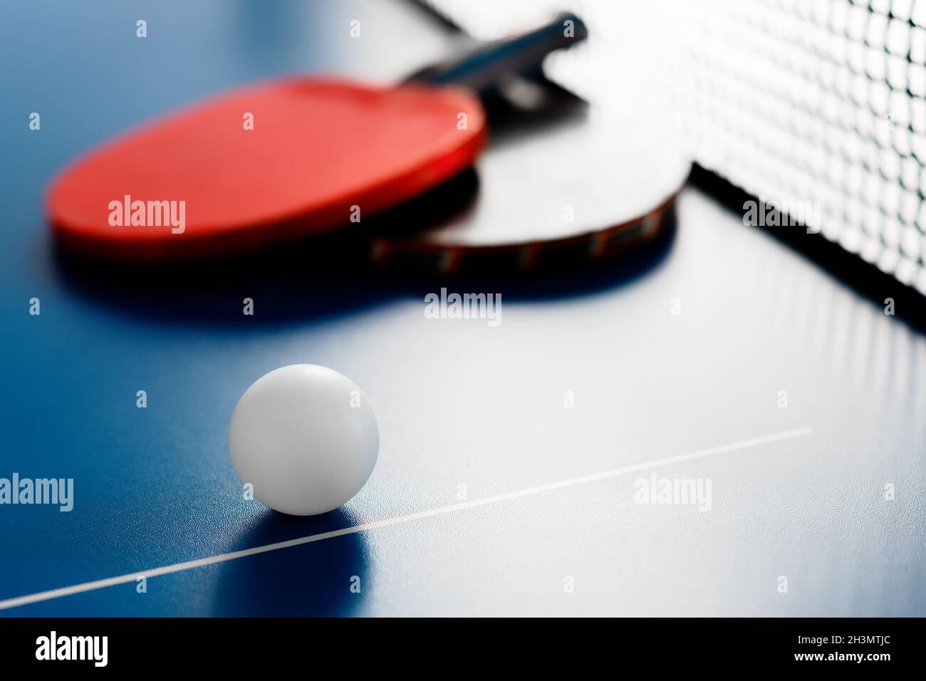 Due racchette da tennis e una palla bianca si trovano su un tavolo da tennis vicino alla rete. Attività ricreative attive e giocare a ping pong. Background sportivo. Foto Stock