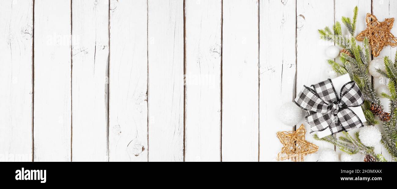 Banner angolo natalizio con rami, ornamenti e in bianco e nero checked bufalo plaid regalo. Vista dall'alto su sfondo di legno bianco con poliziotto Foto Stock