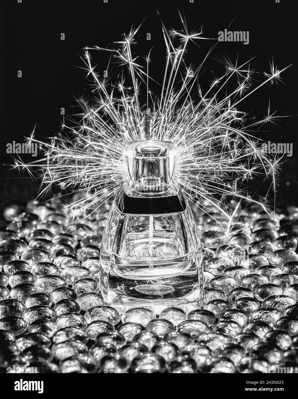 Un luccicante illuminato lancia scintille su una bottiglia di profumo 'vera Wang' seduta su perline di vetro Foto Stock