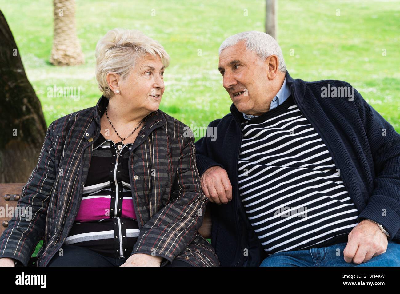 Coppia anziana che parla sul banco del parco. Il marito e la moglie anziano si godono la pensione in giorno di sole all'aperto. Complicità, comprensione reciproca dei concetti Foto Stock