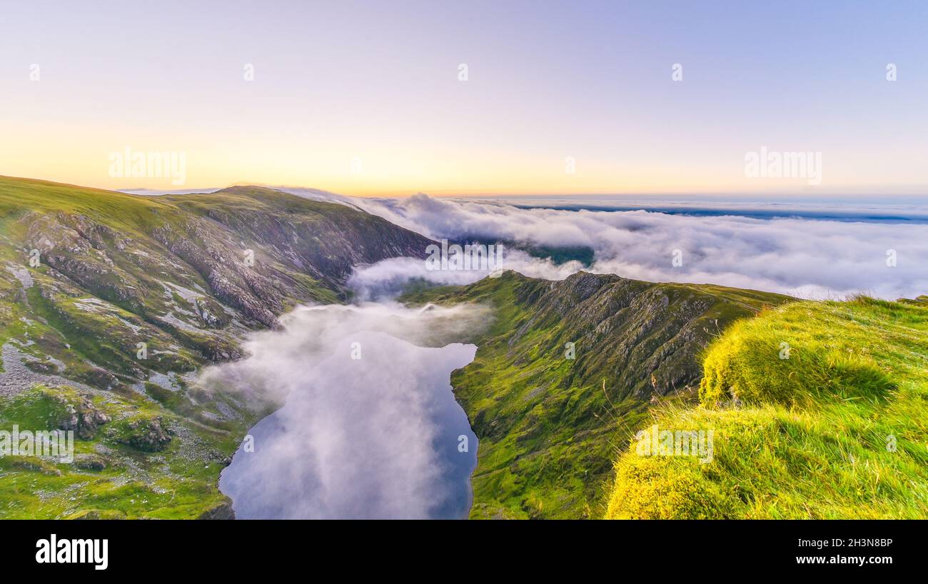 Incredibile alba sul monte Cadair Idris a Snowdonia, nel Galles del Nord. Sole che brilla sul lago glaciale, bella inversione nube avvolge le montagne intorno. Foto Stock